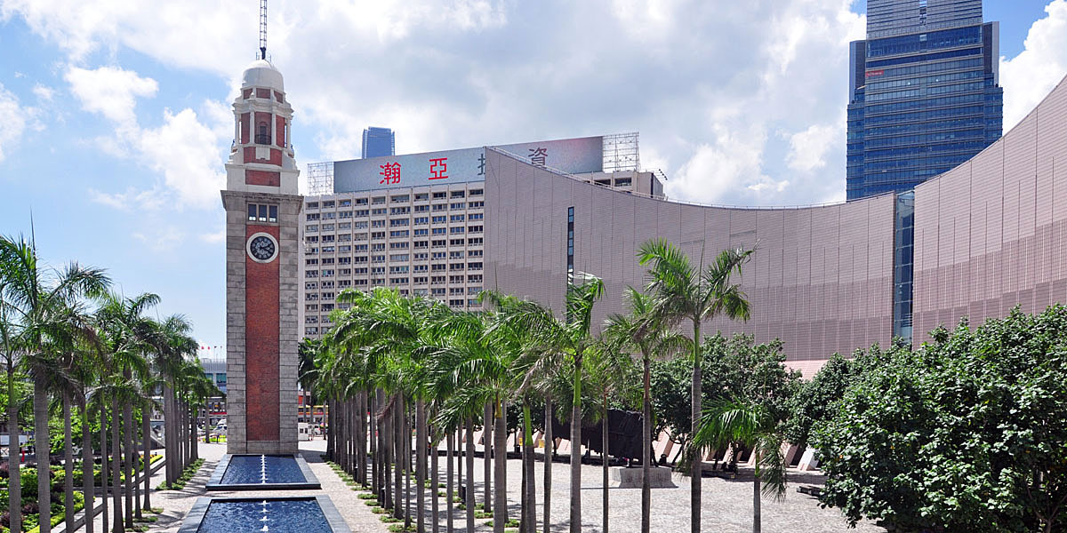 Iconic Tsim Sha Tsui Clock Tower and Hong Kong Cultural Centre along a palm-lined waterfront promenade with modern skyscrapers in the background